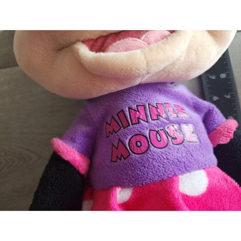 May include: A plush Minnie Mouse toy wearing a purple shirt with the text "Minnie Mouse" in pink letters and a pink and white polka dot skirt.
