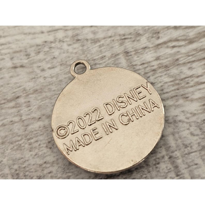 May include: Silver-colored round charm with the text "&copy;2022 DISNEY MADE IN CHINA" on the back.