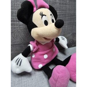 May include: A plush Minnie Mouse doll, featuring a black head and ears, a beige face, and a pink dress with white polka dots. The doll has white gloves and pink shoes. The bow on her head is pink.