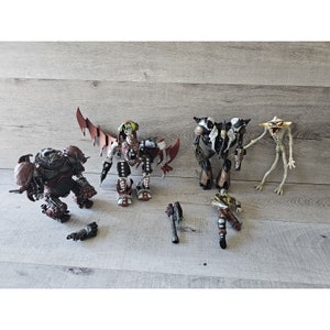 May include: A collection of five action figures from the Spawn franchise. The figures are made of plastic and are painted in various shades of brown, black, and white. The figures are posed in various action poses.