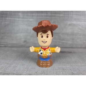 May include: A plastic toy figure of Woody from the animated film Toy Story. The figure has a brown cowboy hat, a yellow shirt with a cow print vest, a blue belt, and brown pants. The figure's arms are outstretched.