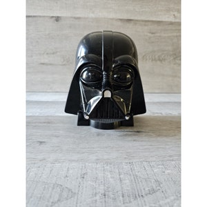 以下が含まれることがあります： 詳細な顔面マスクが付いた黒いプラスチック製のダース・ベイダーのヘルメット。ヘルメットは玩具で、滑らかで光沢のある仕上げになっています。