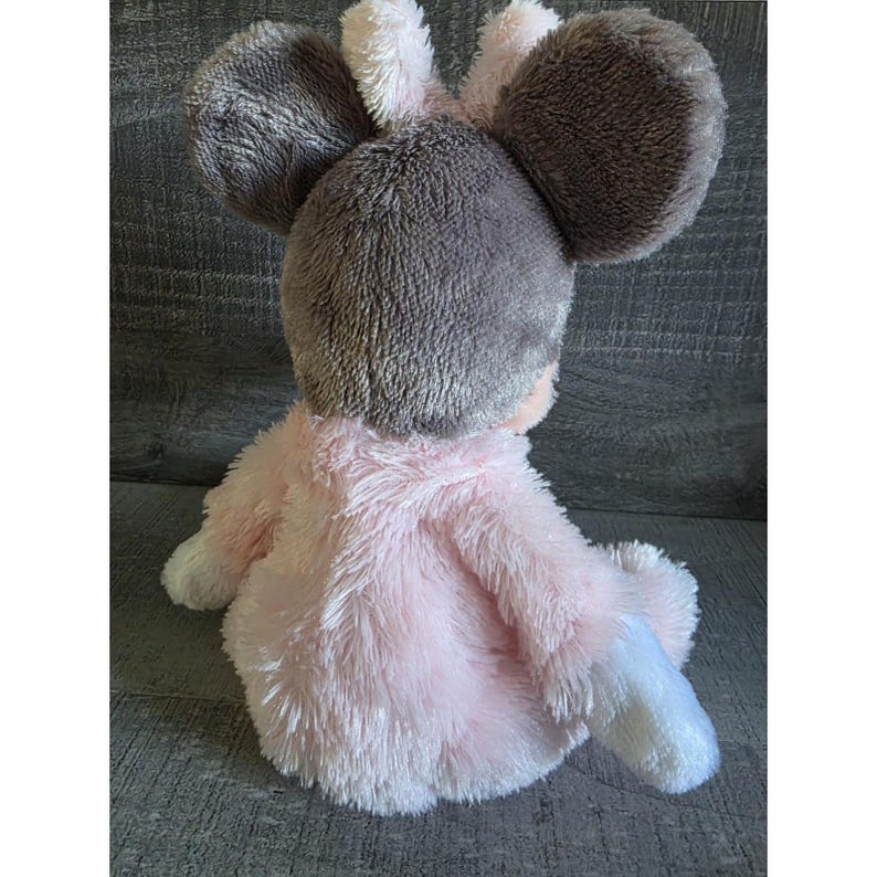 May include: A plush toy mouse with a pink body and a gray head with large ears. The toy is soft and fluffy, with white accents on the feet and ears. The mouse is sitting down.