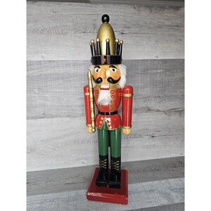 May include: A traditional wooden nutcracker with a red and green uniform, a gold crown, and a white beard. The nutcracker is holding a gold-tipped staff.
