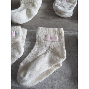 Puede incluir: Un conjunto de calcetines blancos para beb&eacute; con una etiqueta rosa que dice " OshKosh" en un calcet&iacute;n.