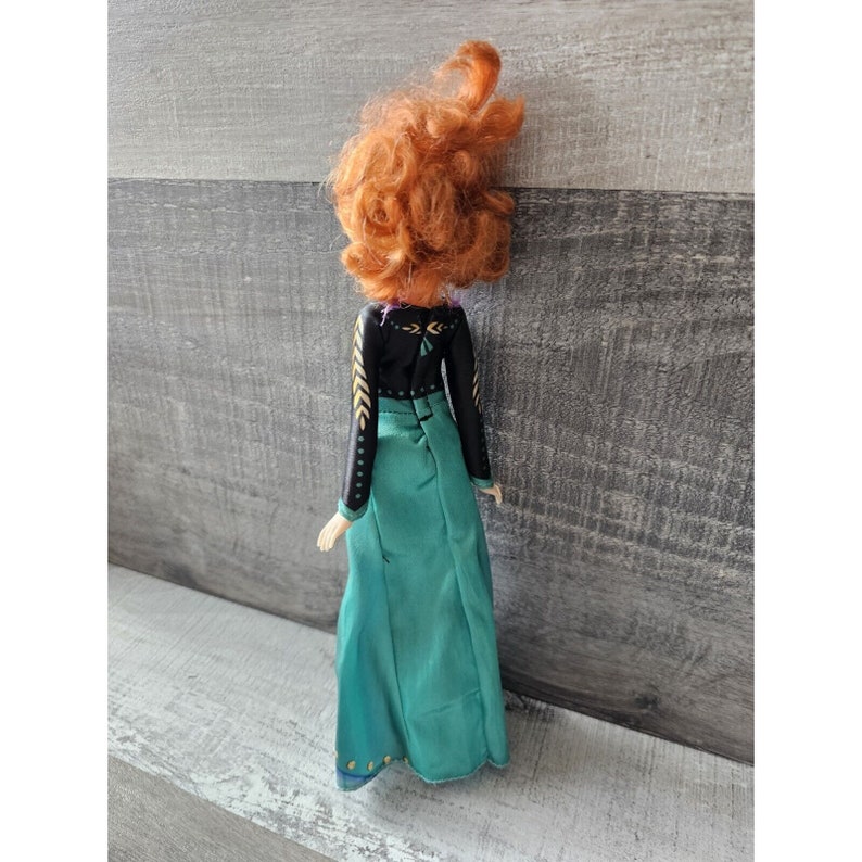 May include: A doll wearing a black and green dress with gold accents. The doll has long, red hair.