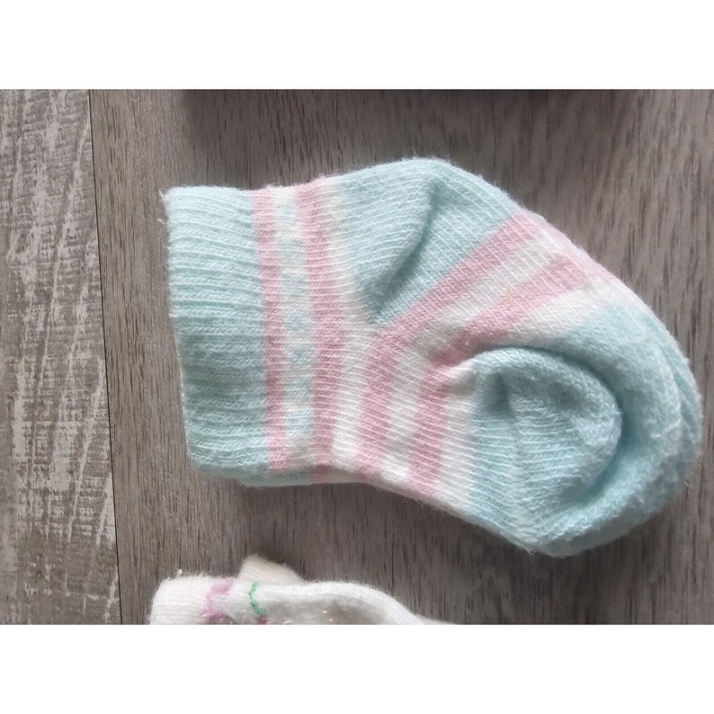 Puede incluir: Un par de calcetines para beb&eacute; con un patr&oacute;n de rayas azul claro y rosa.