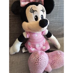 May include: A pink and white polka dot dress with a sparkly pink bow on a plush Minnie Mouse toy.
