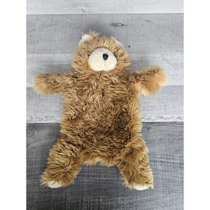 Puede incluir: Una alfombra de oso de peluche marrón con la cara blanca y los ojos negros. La alfombra está hecha de pelo suave y esponjoso y es perfecta para añadir un toque de fantasía a cualquier habitación.