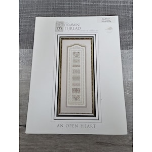Peut inclure: Un schéma de point d'aiguille blanc et or avec une image encadrée d'un motif de point de croix intitulé "Un cœur ouvert". Le schéma est de The Drawn Thread, Charted Needlework Designs.