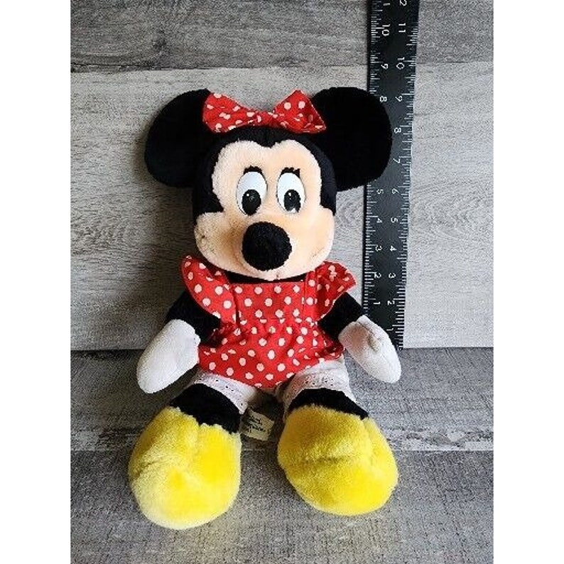 Peut inclure: Un jouet en peluche de Minnie Mouse, la petite amie de Mickey Mouse. Elle porte une robe rouge &agrave; pois blancs et un n&oelig;ud rouge. Elle a des yeux noirs et un nez noir.