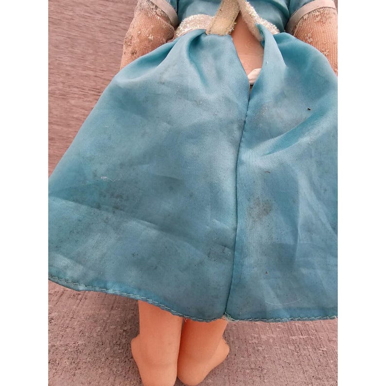 May include: A vintage doll wearing a light blue dress with a white lace trim. The doll has a fabric body and plastic legs and feet.