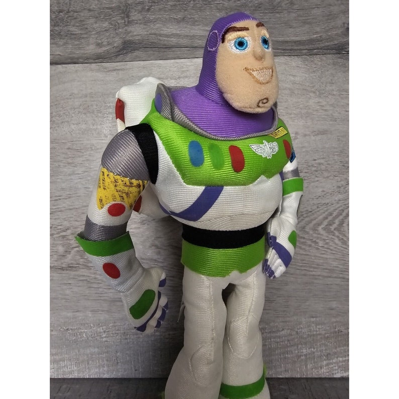 Peut inclure: Un jouet en peluche de Buzz l'&Eacute;clair de la franchise Toy Story. Le jouet porte sa combinaison de ranger spatial signature avec un casque violet, un gilet vert et un pantalon blanc. Il a un visage amical avec des yeux bleus et un sourire.