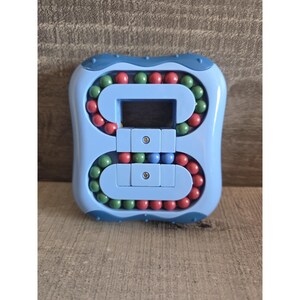 Könnte beinhalten: Ein hellblaues, achtförmiges Puzzlespielzeug mit roten, grünen und blauen Kugeln. Das Spielzeug hat eine quadratische Form mit abgerundeten Kanten und kleinen Metallnieten. Die Kugeln sind in gebogenen Bahnen angeordnet.