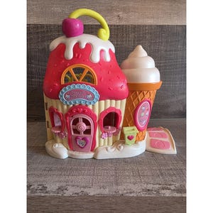May include: A pink and white toy playset resembling a cupcake and ice cream cone. The cupcake features a cherry and the words "Sweet Shoppe". The ice cream cone has a vanilla ice cream scoop.
