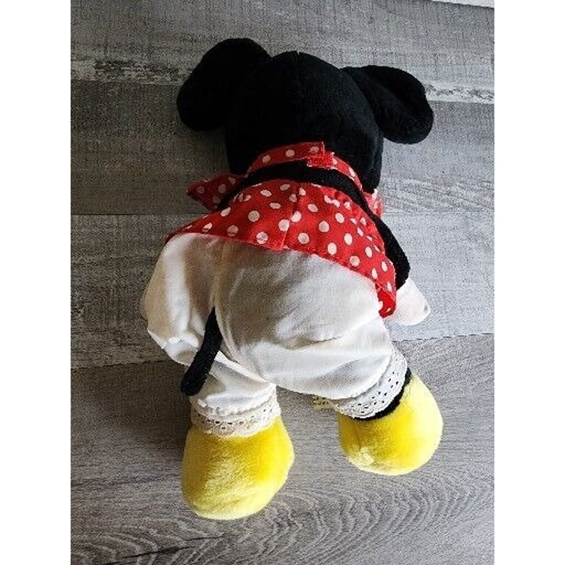 Peut inclure: Un jouet en peluche de Minnie Mouse portant une robe &agrave; pois rouges et blancs avec un n&oelig;ud noir. Le jouet a des oreilles noires, un nez noir et des chaussures jaunes.