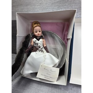 May include: A Madame Alexander "Charmie" doll from The Fashion Collection Platinum, in a white gown with brown embroidery and gloves. The doll has a bun hairstyle and is in a box with a faux fur wrap.