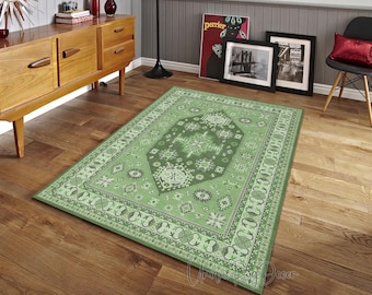 May include: A rectangular green rug with an intricate geometric pattern. The rug features a central medallion design with floral and star motifs, bordered by a repeating pattern. The rug is placed on a hardwood floor, adding a touch of elegance to the room.