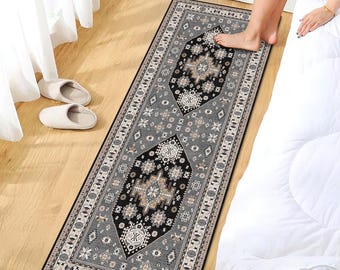 May include: A gray and black patterned runner rug with a geometric design. The rug features a central black medallion with beige and white details, surrounded by a gray border with repeating patterns. The rug is rectangular and placed on a wooden floor.
