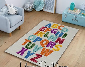 May include: A rectangular rug with the alphabet in various colors, including blue, orange, green, and purple. The rug is on a light-colored floor. The text "Unique Rug Decor" is at the bottom of the rug.