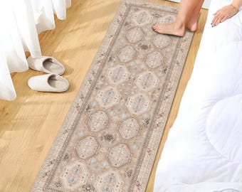 May include: A rectangular beige rug with an intricate geometric pattern, featuring shades of tan, cream, and light blue. The rug is placed on a wooden floor, next to a bed with white bedding. The rug's design includes repeating medallion shapes and decorative borders.