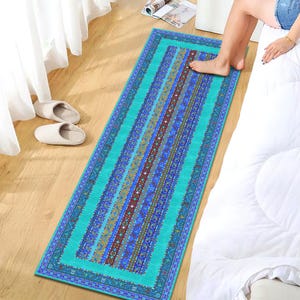 May include: A rectangular turquoise rug with a detailed pattern of vertical stripes in shades of blue, brown, and gold. The rug has a border and is placed on a wooden floor. The rug is approximately 60 inches long.
