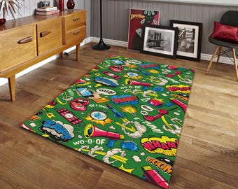 May include: A rectangular green rug with a comic book style design. The rug features various speech bubbles with words like "ZAP" and "BOOM", along with images of a phone, a rocket, and a megaphone. The rug is placed on a wooden floor.