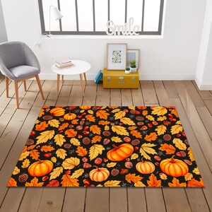 Op de afbeelding: Een rechthoekig vloerkleed met een zwarte achtergrond, versierd met een herhalend patroon van oranje pompoenen, gele en oranje bladeren, eikels en dennenappels. Dit vloerkleed voor binnen is ontworpen om een seizoensgebonden gevoel aan elke kamer te geven.