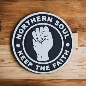 May include: A black and white circular sign with the text "Northern Soul Keep The Faith" and a raised fist in the center.