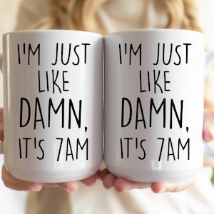May include: Two white coffee mugs with black text. The text on the mugs reads "I'm just like damn, it's 7am".