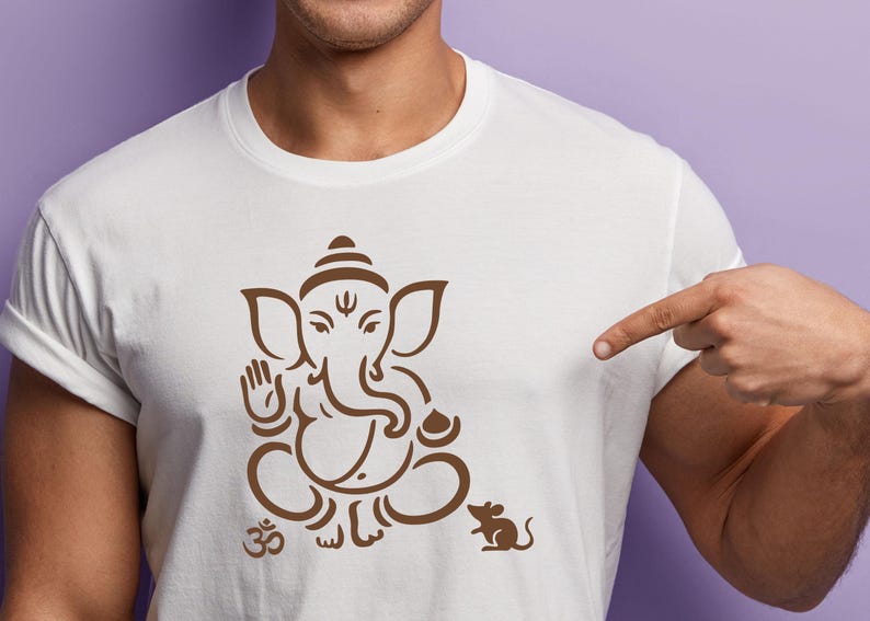 May include: White t-shirt featuring a brown illustration of the Hindu deity Ganesha in a seated pose, with an Om symbol and a mouse. The design is centered on the shirt.