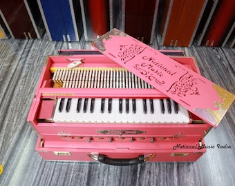 May include: A pink harmonium with a carved wooden lid that says "National Music". The harmonium has a white keyboard and a carrying handle.