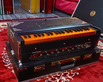 May include: A black harmonium with orange keys and a decorative carved wooden top. The harmonium is in a black carrying case with a handle and a combination lock.