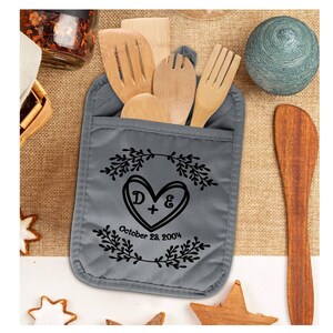 May include: Gray oven mitt with a pocket for utensils. The mitt has a black design of a heart with the initials D & E and the date October 28, 2004.