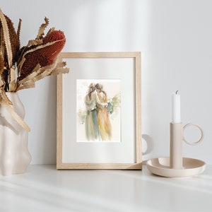May include: A framed watercolor painting of two women embracing, with a soft, muted color palette of greens, yellows, and browns. The painting is set against a white background and is displayed on a white shelf with a candle and vase of dried flowers.