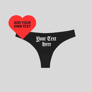May include: Black thong underwear with the text "Your Text Here" in a gothic font. A red heart shape with the text "Add Your Own Text" is in the upper left corner. The background is a light gray.