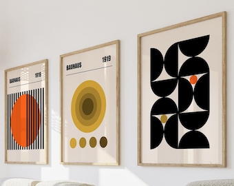 Könnte beinhalten: Drei gerahmte Bauhaus-Kunstdrucke mit geometrischen Designs in Orange, Schwarz und Gelb. Die Drucke werden über einem hellfarbigen Ecksofa ausgestellt. Der Text "Bauhaus 1919" ist auf jedem Druck zu sehen. Eine gewebte Pendelleuchte hängt von der Decke.