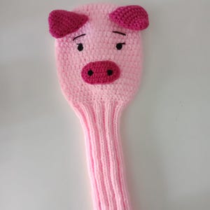 May include: Pink knitted golf club head cover shaped like a pig with pink ears and a black embroidered snout.
