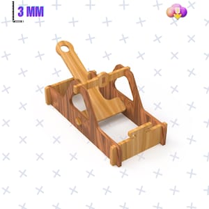 Puede incluir: Un modelo de catapulta de madera con tonos marrón claro y oscuro. El modelo tiene una palanca, una plataforma de lanzamiento y una base. El texto "3 MM" es visible en la esquina superior izquierda.