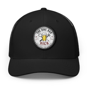 May include: A black trucker hat featuring a circular patch on the front. The patch displays a beer mug graphic with the text THE DIVE BAR, EST. 2020, and DICK, along with the phrase FINDING AMERICA'S BEST BAD BARS in a distressed, vintage style.