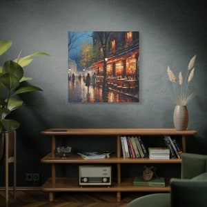 Puede incluir: Una pintura de una escena callejera parisina de noche. La calle est&aacute; mojada por la lluvia y hay gente caminando por un caf&eacute; con mesas y sillas afuera. El caf&eacute; tiene un toldo rojo y luces amarillas c&aacute;lidas en el interior.