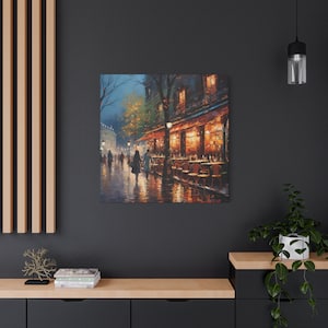 Puede incluir: Una pintura de una escena callejera parisina de noche, con un caf&eacute; con mesas y sillas afuera. El caf&eacute; est&aacute; iluminado con luces amarillas c&aacute;lidas, y hay gente caminando. La calle est&aacute; mojada por la lluvia, y los edificios son oscuros y misteriosos.