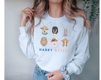 May include: Light blue sweatshirt with a graphic print of six animal faces wearing hats and accessories. The text "HARRY STYLES" is printed below the animal faces.