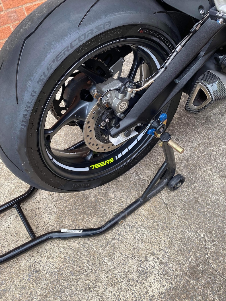 Puede incluir: Una motocicleta negra con un neum&aacute;tico trasero negro y un caballete trasero negro. El neum&aacute;tico tiene una franja blanca y el texto "Diablo Supercorsa 120/70 ZR17 58W" impreso en el lateral. El neum&aacute;tico tambi&eacute;n tiene una franja amarilla con el texto "765RS" impreso en &eacute;l.