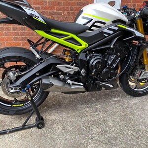 Puede incluir: Una motocicleta negra y plateada con detalles verdes y blancos. La motocicleta tiene un tubo de escape negro y un asiento negro. La motocicleta est&aacute; en un soporte de motocicleta.