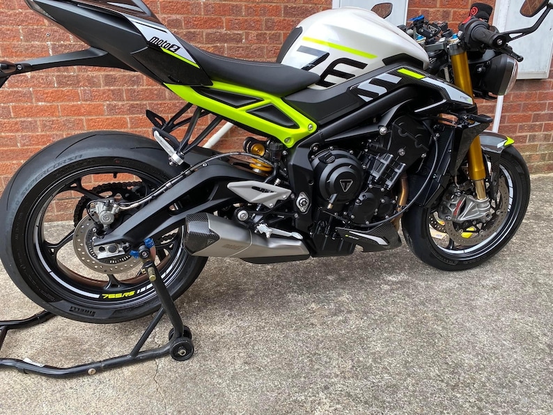 Puede incluir: Una motocicleta negra y plateada con detalles verdes y blancos. La motocicleta tiene un tubo de escape negro y un asiento negro. La motocicleta est&aacute; en un soporte de motocicleta.