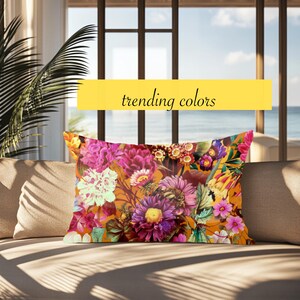 May include: Rectangular decorative pillow with a vibrant floral pattern in shades of pink, purple, yellow, and white on an orange background. The pillow is on a beige sofa, with the text "trending colors" in a yellow banner.