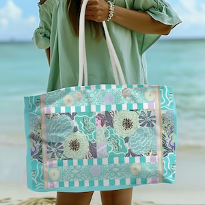May include: A turquoise and white striped tote bag with a floral pattern. The bag has a white rope handle and is made of canvas.