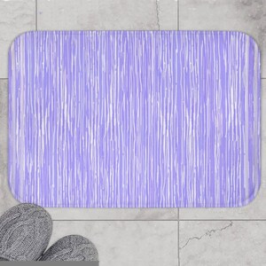 May include: A rectangular bath mat featuring a light purple background with a pattern of thin, vertical white lines of varying lengths and thicknesses that create a textured, abstract appearance across the entire surface of the mat.