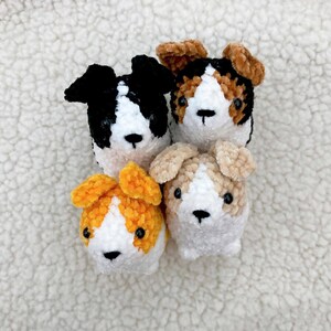 May include: Four handmade plush dog toys in various colors: black and white, brown and white, orange and white, and tan and white. Each toy has a white face and body, with black button eyes and a black nose. The toys are made of a soft, textured material.